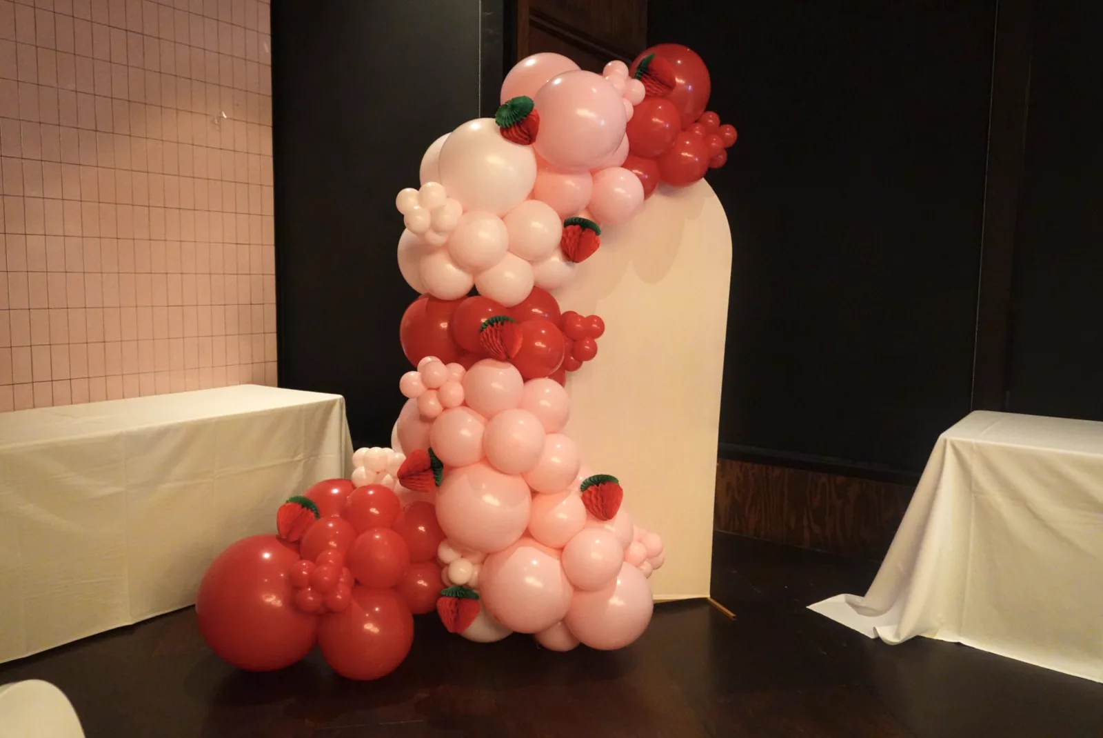 Strawberry balloon garland on a cream arch backdrop for a first birthday