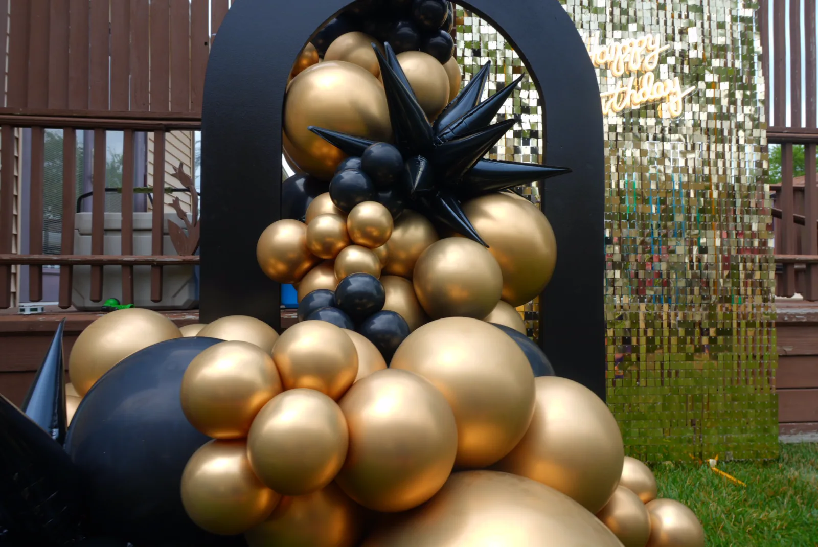 Black and gold balloon garland on an arch backdrop with a gold sequin wall