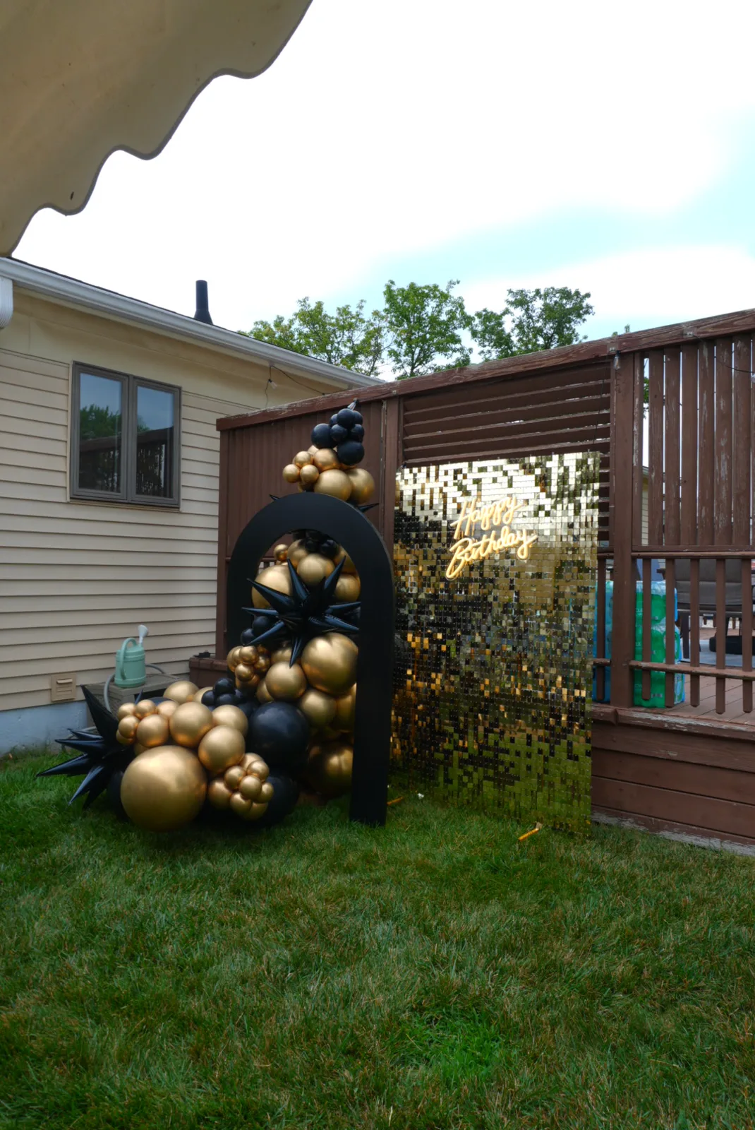 Black and gold balloon arch with starburst accents set up in a backyard