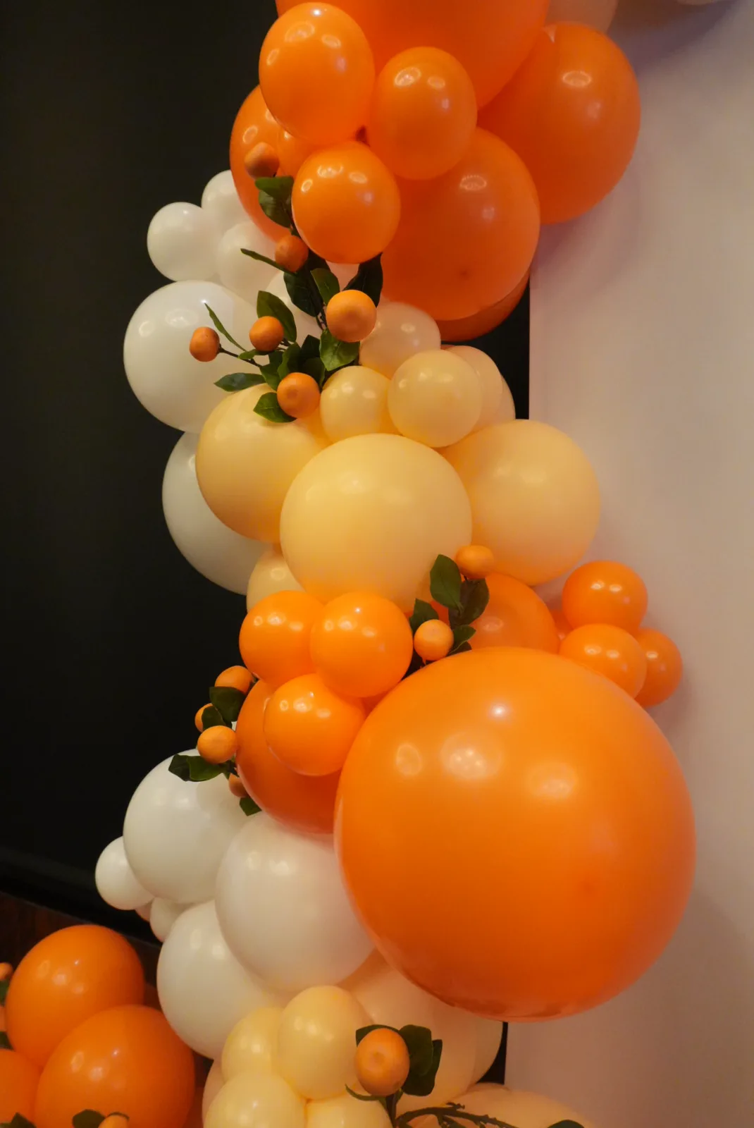 Close-up of an orange and ivory balloon garland trimmed with citrus and greenery