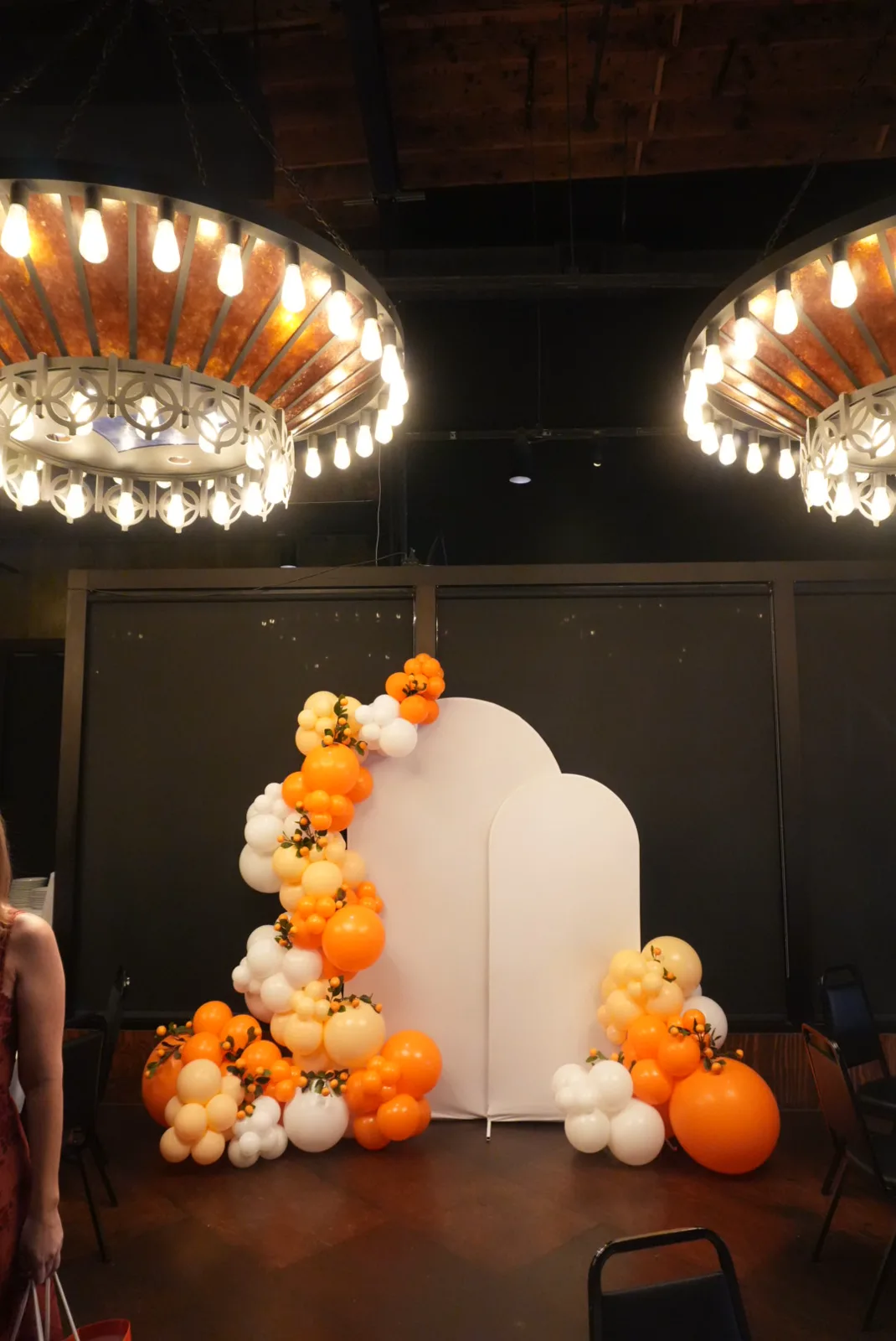 Orange and ivory balloon arch in an event venue beneath chandeliers