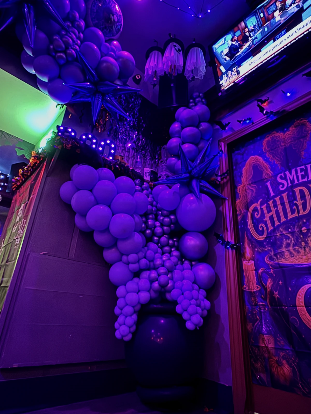 Halloween balloon installation in purple light with starburst accents and a balloon cauldron at a bar